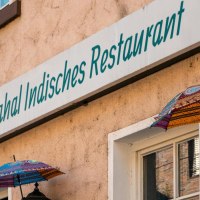 Fassade eines indischen Restaurants in Stuttgart mit bunten Schirmen und einem Schild mit der Aufschrift 'Taj Mahal Indisches Restaurant'., &copy; SMG, Sarah Schmid