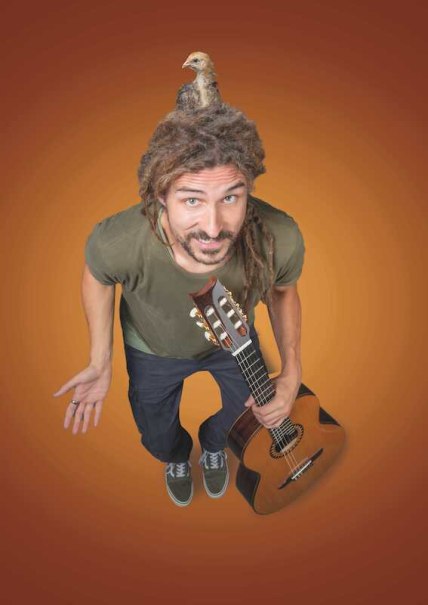 Ein Mann mit Dreadlocks hält eine Gitarre und hat einen kleinen Vogel auf dem Kopf. Er trägt ein grünes T-Shirt und steht vor einem orangefarbenen Hintergrund., © Rosenau Kultur e.V. Ein Mann mit Dreadlocks hält eine Gitarre und hat einen kleinen Vogel auf dem Kopf. Er trägt ein grünes T-Shirt und steht vor einem orangefarbenen Hintergrund., © Rosenau Kultur e.V.