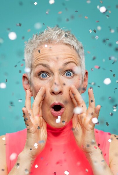 Person mit kurzem Haar und &uuml;berraschter Mimik, umgeben von Konfetti vor blauem Hintergrund., &copy; Renitenztheater Stuttgart e.V.