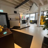 Modern reception area with counter, chairs and plants. Bright lighting and decorations create an inviting atmosphere., © pause & play Stuttgart Modern reception area with counter, chairs and plants. Bright lighting and decorations create an inviting atmosphere., © pause & play Stuttgart