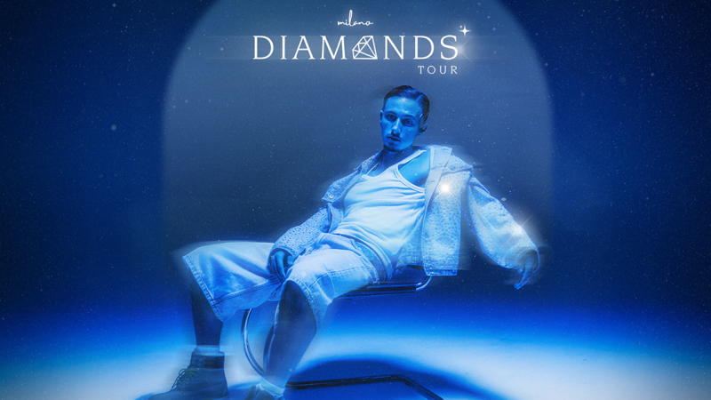 Ein Mann in weißer Kleidung sitzt lässig auf einem Stuhl in einer blauen, futuristischen Umgebung. Oben ist der Schriftzug 'Milano Diamonds Tour' zu sehen., © links im Bild Ein Mann in weißer Kleidung sitzt lässig auf einem Stuhl in einer blauen, futuristischen Umgebung. Oben ist der Schriftzug 'Milano Diamonds Tour' zu sehen., © links im Bild