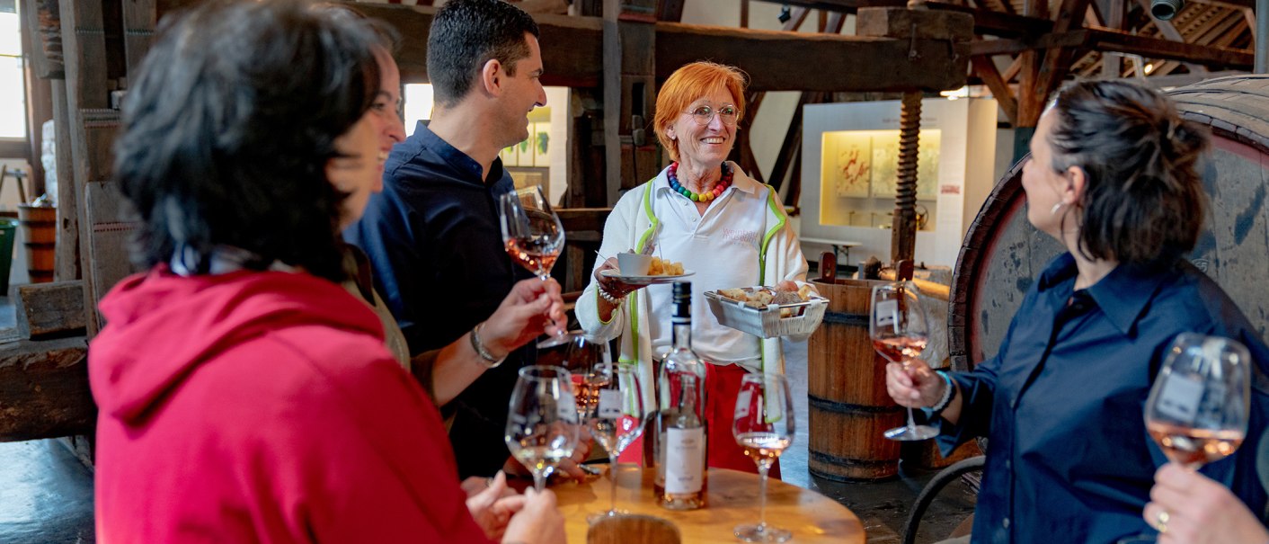 Eine Gruppe von Menschen genießt eine Weinprobe im Weinbaumuseum. Eine Frau serviert Snacks, während die anderen Wein in Gläsern halten., © Stuttgart-Marketing GmbH, Thomas Niedermüller