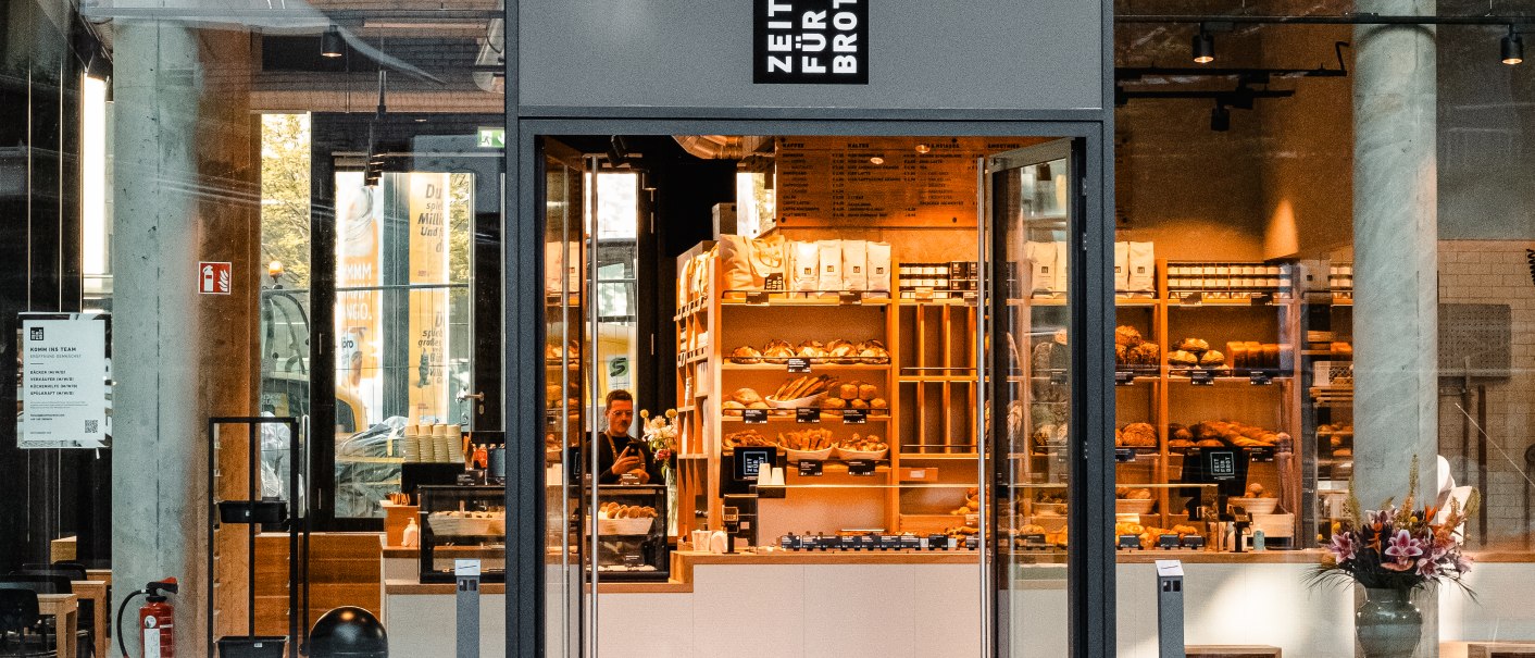 Eingang einer Bäckerei mit Glasfront. Im Inneren sind Regale mit Backwaren zu sehen. Über der Tür steht 'Zeit für Brot'., © Zeit für Brot Stuttgart Eingang einer Bäckerei mit Glasfront. Im Inneren sind Regale mit Backwaren zu sehen. Über der Tür steht 'Zeit für Brot'., © Zeit für Brot Stuttgart