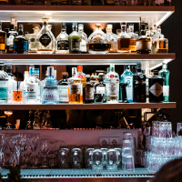 Bar mit beleuchteten Regalen voller Spirituosenflaschen, Gläsern und einem Barkeeper im Hintergrund. Gemütliche Atmosphäre mit gedämpftem Licht., © SMG, Sarah Schmid Bar mit beleuchteten Regalen voller Spirituosenflaschen, Gläsern und einem Barkeeper im Hintergrund. Gemütliche Atmosphäre mit gedämpftem Licht., © SMG, Sarah Schmid