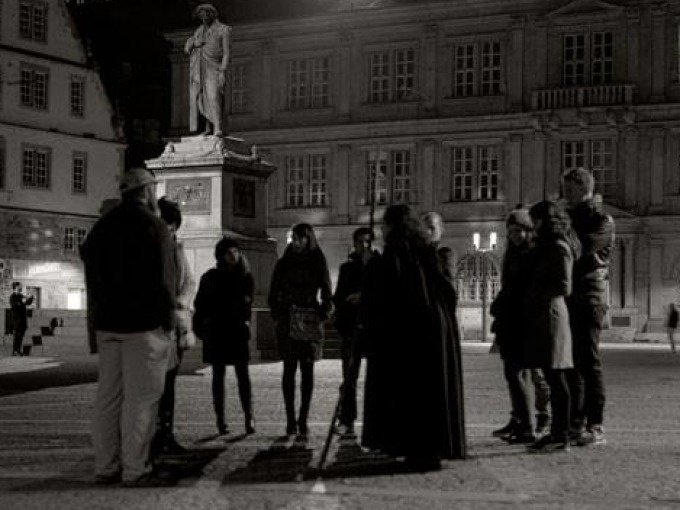 Eine Gruppe von Menschen steht nachts vor einer Statue auf einem Platz in Stuttgart. Die Szene wirkt geheimnisvoll und historisch., © Stuttgarter Geister Eine Gruppe von Menschen steht nachts vor einer Statue auf einem Platz in Stuttgart. Die Szene wirkt geheimnisvoll und historisch., © Stuttgarter Geister