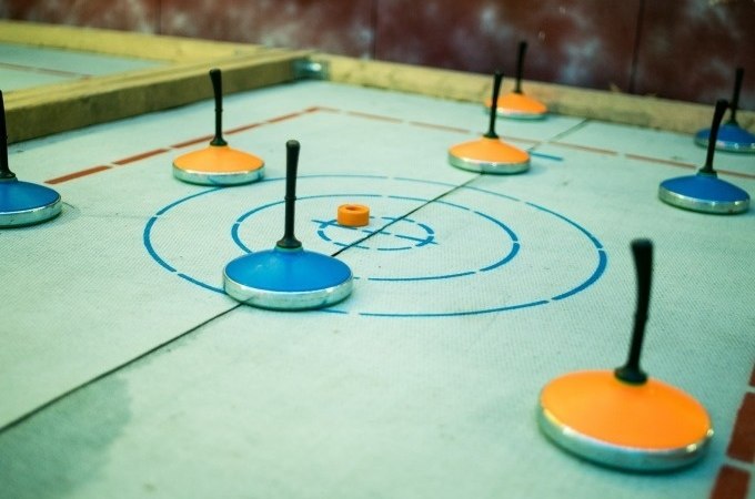 Eisstöcke in Blau und Orange liegen auf einer Zielscheibe beim Eisstockschießen. Der Boden ist markiert und die Stöcke sind verteilt., © Cool-Tours StattReisen Eisstöcke in Blau und Orange liegen auf einer Zielscheibe beim Eisstockschießen. Der Boden ist markiert und die Stöcke sind verteilt., © Cool-Tours StattReisen