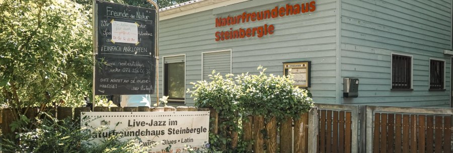 The NaturFreundeHaus Steinbergle with a sign announcing live jazz, surrounded by plants and a wooden fence., &copy; NaturFreundehaus Steinbergle, Stuttgart
