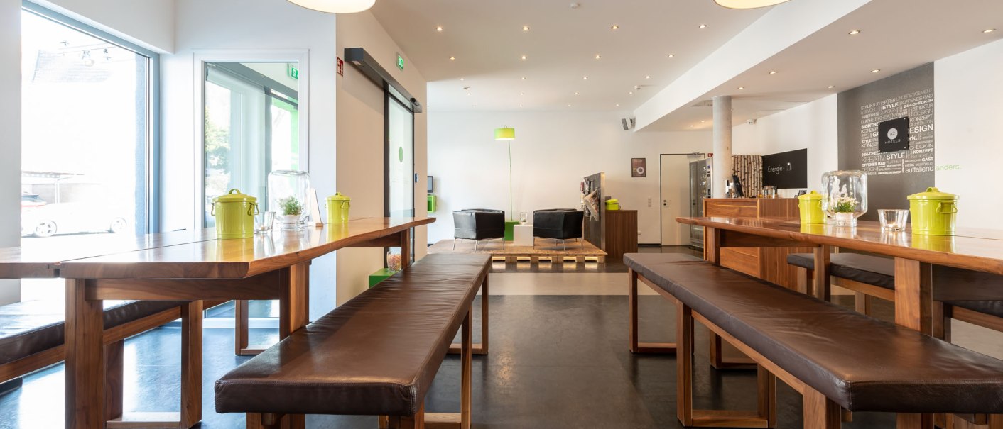 Modern lobby with wooden tables and benches, large lamps and a seating area in the background. Bright, inviting atmosphere., &copy; a2 HOTELS