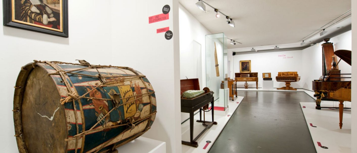 Museum exhibition with historical musical instruments, including a painted drum in the foreground and various keyboard instruments in the background., &copy; Landesmuseum W&uuml;rttemberg