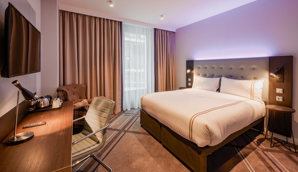 Modern hotel room with large bed, desk, armchair and TV. Subtle lighting and neutral colors create an inviting atmosphere., © Premier Inn Modern hotel room with large bed, desk, armchair and TV. Subtle lighting and neutral colors create an inviting atmosphere., © Premier Inn