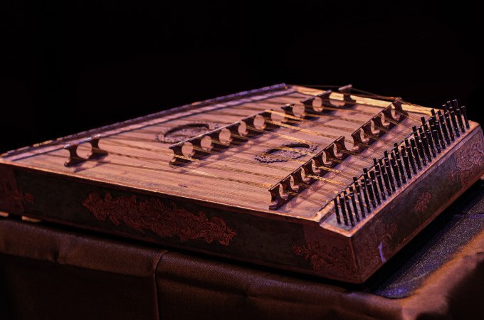 Ein traditionelles Saiteninstrument mit mehreren Saiten und Verzierungen, auf einem Tisch platziert, vor einem dunklen Hintergrund., © Landesmuseum Württemberg Ein traditionelles Saiteninstrument mit mehreren Saiten und Verzierungen, auf einem Tisch platziert, vor einem dunklen Hintergrund., © Landesmuseum Württemberg