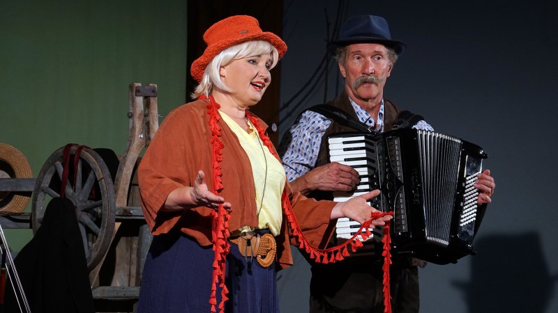 Eine Frau mit rotem Hut singt, w&auml;hrend ein Mann neben ihr Akkordeon spielt. Im Hintergrund sind Wagenr&auml;der zu sehen., &copy; Katja Ritter
