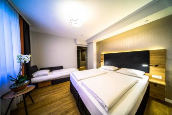 Modern double room with double bed, single bed, wooden floor and orchid on a table., © PLAZA INN Rieker Stuttgart Hauptbahnhof