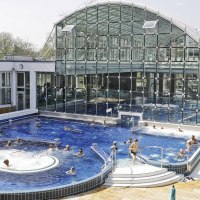Das SoleBad Bad Cannstatt zeigt ein modernes Schwimmbecken mit Glasfassade. Menschen entspannen im Wasser und auf Liegestühlen., © Stuttgarter Bäder Das SoleBad Bad Cannstatt zeigt ein modernes Schwimmbecken mit Glasfassade. Menschen entspannen im Wasser und auf Liegestühlen., © Stuttgarter Bäder