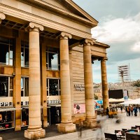 Eingang der Königsbau Passagen mit imposanten Säulen. Menschen bewegen sich auf dem Platz davor. Im Hintergrund ist eine Baustelle sichtbar., © Königsbau Eingang der Königsbau Passagen mit imposanten Säulen. Menschen bewegen sich auf dem Platz davor. Im Hintergrund ist eine Baustelle sichtbar., © Königsbau