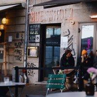 Exterior view of the 'Suessholz' caf&eacute; in the Leonhardsviertel. People are sitting outside, chatting. Graffiti on the walls, neon light in the window., &copy; &copy; Stuttgart-Marketing GmbH, Alwin Maigler