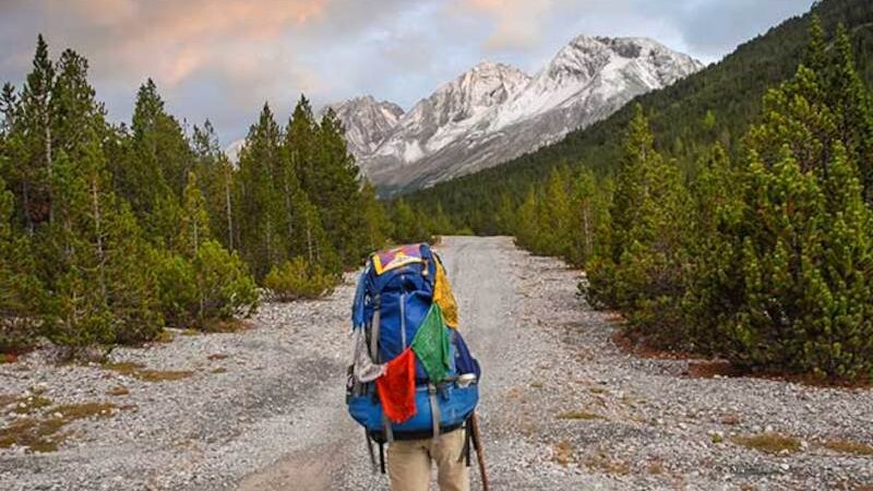 A person with a large rucksack hikes along a gravel path through a wooded mountain landscape at sunset., &copy; Theaterhaus Stuttgart e.V.