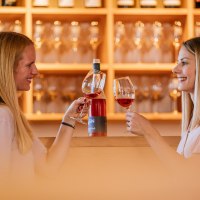 Two women clink glasses of wine in a wine shop. Wine bottles and glasses can be seen in the background., &copy; Stuttgart-Marketing GmbH, Thomas Niederm&uuml;ller