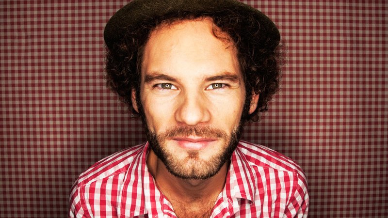 Ein Mann mit einem Hut und einem rot-weiß karierten Hemd steht vor einem passenden karierten Hintergrund und schaut direkt in die Kamera., © Renitenztheater Stuttgart e.V. Ein Mann mit einem Hut und einem rot-weiß karierten Hemd steht vor einem passenden karierten Hintergrund und schaut direkt in die Kamera., © Renitenztheater Stuttgart e.V.