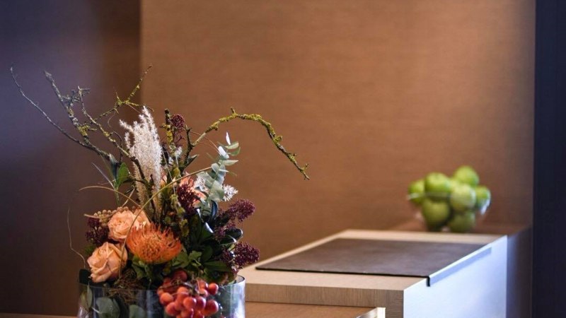 Elegante Rezeption mit Blumenarrangement und modernen Hängelampen. Im Hintergrund eine Schale mit grünen Äpfeln., © TOMAS Elegante Rezeption mit Blumenarrangement und modernen Hängelampen. Im Hintergrund eine Schale mit grünen Äpfeln., © TOMAS