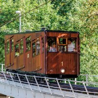 Eine historische Standseilbahn mit Holzverkleidung f&auml;hrt eine geneigte Strecke entlang, umgeben von dichtem Gr&uuml;n., &copy; TMBW, Gregor Lengler