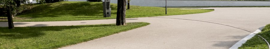 Ein gepflegter Park mit geschwungenen Gehwegen, Bäumen und modernen Wohngebäuden im Hintergrund. Ein Gedenkstein ist sichtbar., © Foto-Kunst Andreas Keller
