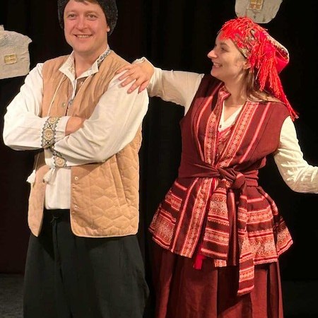 Zwei Personen in traditioneller ukrainischer Kleidung stehen lächelnd auf einer Bühne. Der Mann trägt eine Mütze, die Frau ein rotes Kopftuch., © Theater Atelier Zwei Personen in traditioneller ukrainischer Kleidung stehen lächelnd auf einer Bühne. Der Mann trägt eine Mütze, die Frau ein rotes Kopftuch., © Theater Atelier