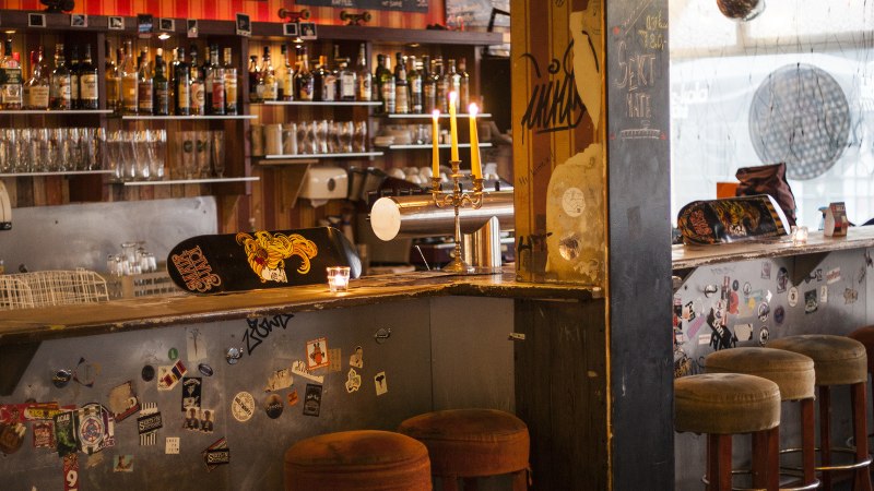 Eine gem&uuml;tliche Bar mit Skateboard-Dekor auf der Theke, Kerzenleuchter und Barhockern. Im Hintergrund sind Flaschen und Gl&auml;ser zu sehen., &copy; Mata Hari, Stuttgart