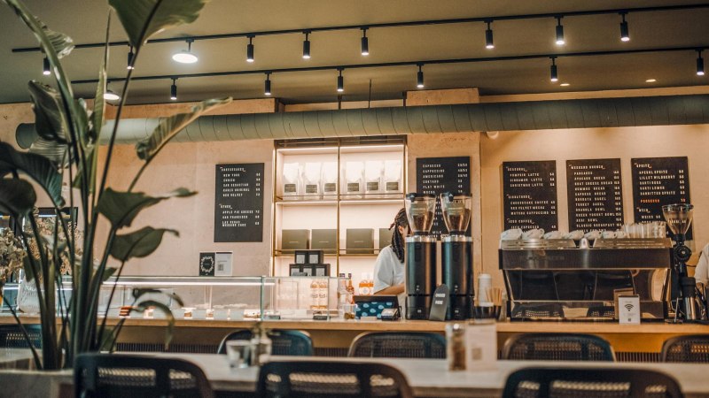 Modern caf&eacute; with counter, coffee machine and menus on the wall. Plants in the foreground, cozy atmosphere., &copy; Maison Karl, Stuttgart