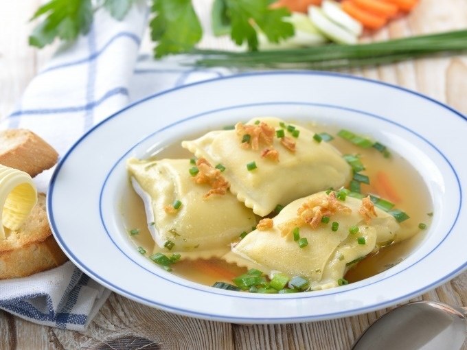 Drei Maultaschen in klarer Br&uuml;he, garniert mit Schnittlauch und R&ouml;stzwiebeln. Im Hintergrund Brot mit Butter und frische Kr&auml;uter., &copy; Cool-Tours StattReisen