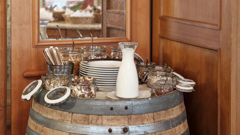 Ein Frühstücksbuffet auf einem Weinfass mit Milch, Nüssen, Besteck und Tellern in einem rustikalen Restaurant., © Badhotel Restaurant Stauferland Ein Frühstücksbuffet auf einem Weinfass mit Milch, Nüssen, Besteck und Tellern in einem rustikalen Restaurant., © Badhotel Restaurant Stauferland