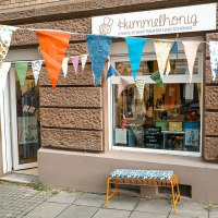 Ladenfront von Hummelhonig mit bunten Wimpeln und einer Bank. Schaufenster zeigt Stoffe und Schnittmuster. Schild der Steuerkanzlei Wanner daneben., &copy; Lena Beck, Hummelkonig GbR, Stuttgart