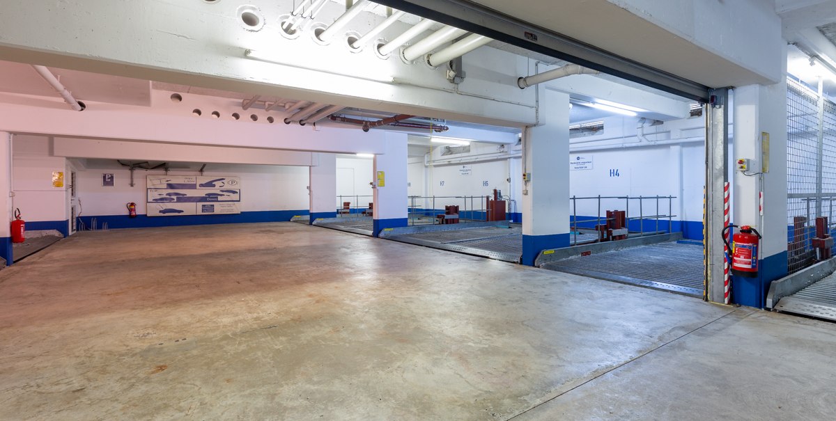 Leere Tiefgarage mit markierten Parkpl&auml;tzen, wei&szlig;en W&auml;nden und blauen Akzenten. Ein Feuerl&ouml;scher ist an der Wand befestigt., &copy; TOMAS