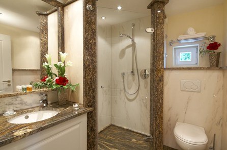 An elegant bathroom with marble tiles, a shower, a sink, and a toilet. Decorated with red flowers and towels., © Jeanette Bender An elegant bathroom with marble tiles, a shower, a sink, and a toilet. Decorated with red flowers and towels., © Jeanette Bender