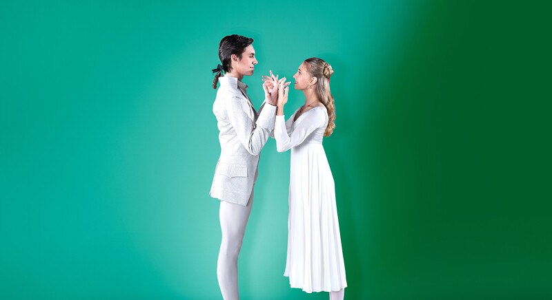 Zwei Balletttänzer in weißen Kostümen stehen sich vor einem grünen Hintergrund gegenüber, in einer eleganten Pose., © Württembergische Staatstheater Stuttgart Zwei Balletttänzer in weißen Kostümen stehen sich vor einem grünen Hintergrund gegenüber, in einer eleganten Pose., © Württembergische Staatstheater Stuttgart
