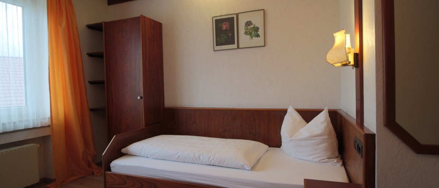 A cozy single room with wooden furniture, a single bed, orange curtains and two murals. A lamp illuminates the room., © TOMAS A cozy single room with wooden furniture, a single bed, orange curtains and two murals. A lamp illuminates the room., © TOMAS