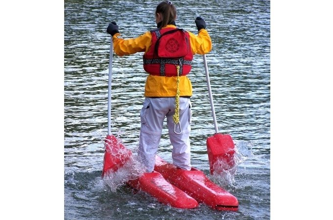 Person mit gelber Jacke und roter Schwimmweste steht auf roten Wasserschuhen im Wasser und h&auml;lt zwei St&ouml;cke., &copy; Cool-Tours StattReisen