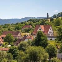 A picturesque village with traditional half-timbered houses, surrounded by green hills and trees, under a clear blue sky., &copy; &copy; Stuttgart-Marketing GmbH