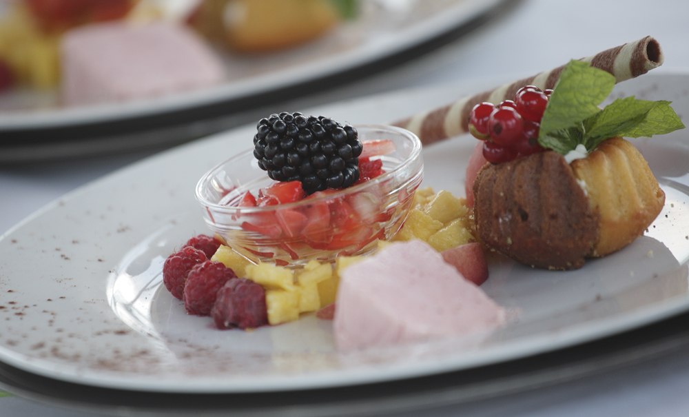 Ein Dessertteller mit Beeren, einem kleinen Kuchen, Schokoladenröllchen und Minzblättern, kunstvoll angerichtet auf einem weißen Teller., © Badhotel Restaurant Stauferland