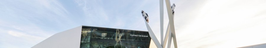 The Porsche Museum with its modern architecture and a sculpture of three cars on high pillars against a blue sky., © Porsche AG, Sabine Braun