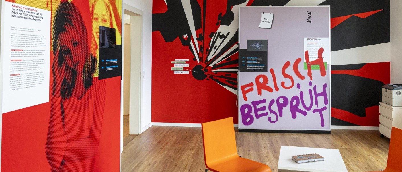 Bunter Ausstellungsraum mit Texten und Grafiken zur Psychologie. Ein orangefarbener Stuhl und ein Tisch mit einem Buch sind sichtbar., © Stuttgart-Marketing GmbH, Sarah Schmid