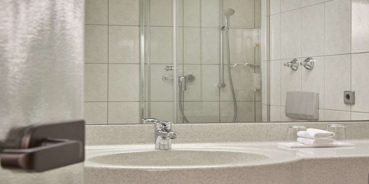 A modern bathroom with a washbasin, a mirror and a shower with a glass door. Towels and glasses are placed on the washbasin., © © H-Hotels.com A modern bathroom with a washbasin, a mirror and a shower with a glass door. Towels and glasses are placed on the washbasin., © © H-Hotels.com