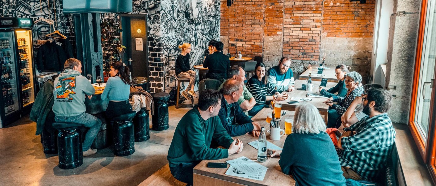 Gem&uuml;tliche Bar mit Backsteinw&auml;nden und Graffiti-Kunst. Menschen sitzen an Tischen, unterhalten sich und genie&szlig;en Getr&auml;nke., &copy; Kraftpaule, Stuttgart