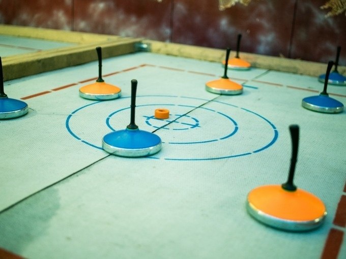 Eisstöcke in Blau und Orange liegen auf einer Zielscheibe beim Eisstockschießen. Der Boden ist markiert und die Stöcke sind verteilt., © Cool-Tours StattReisen