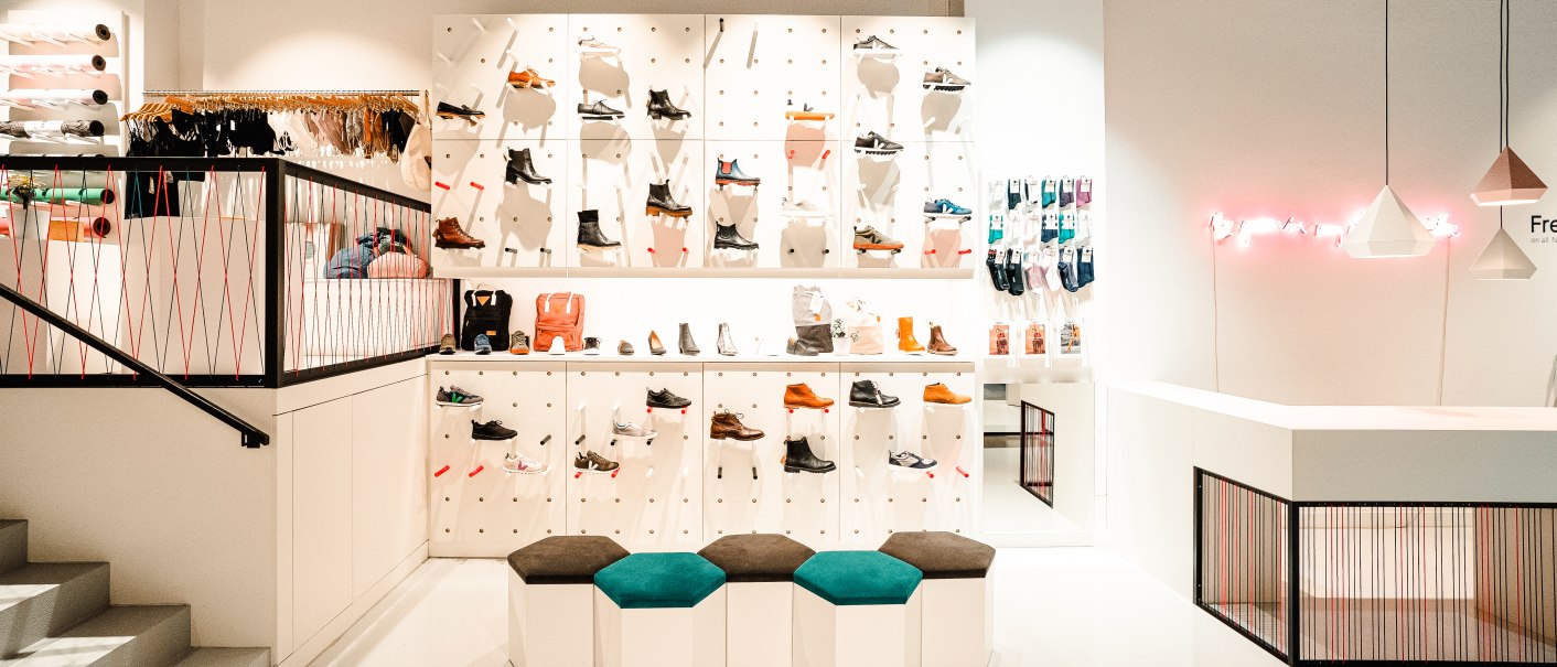 Modernes Schuhgeschäft mit weißen Wänden, Regalen voller Schuhe und bunter Dekoration. Sitzgelegenheiten und ein heller Tresen sind sichtbar., © Elisa Mauruschat Modernes Schuhgeschäft mit weißen Wänden, Regalen voller Schuhe und bunter Dekoration. Sitzgelegenheiten und ein heller Tresen sind sichtbar., © Elisa Mauruschat