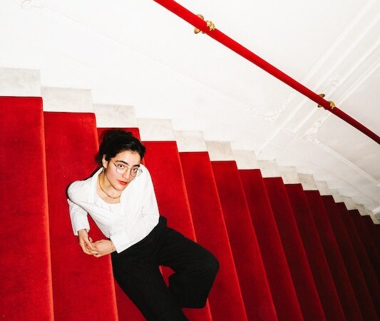 A person in a white shirt and black trousers is lying relaxed on a red staircase with a red banister., &copy; Rosenau Kultur e.V.