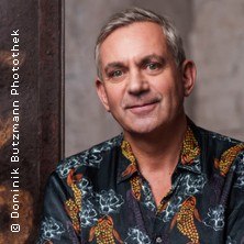 Ein Mann mit grauen Haaren trägt ein bunt gemustertes Hemd und lächelt in die Kamera. Der Hintergrund ist neutral gehalten., © links im Bild Ein Mann mit grauen Haaren trägt ein bunt gemustertes Hemd und lächelt in die Kamera. Der Hintergrund ist neutral gehalten., © links im Bild