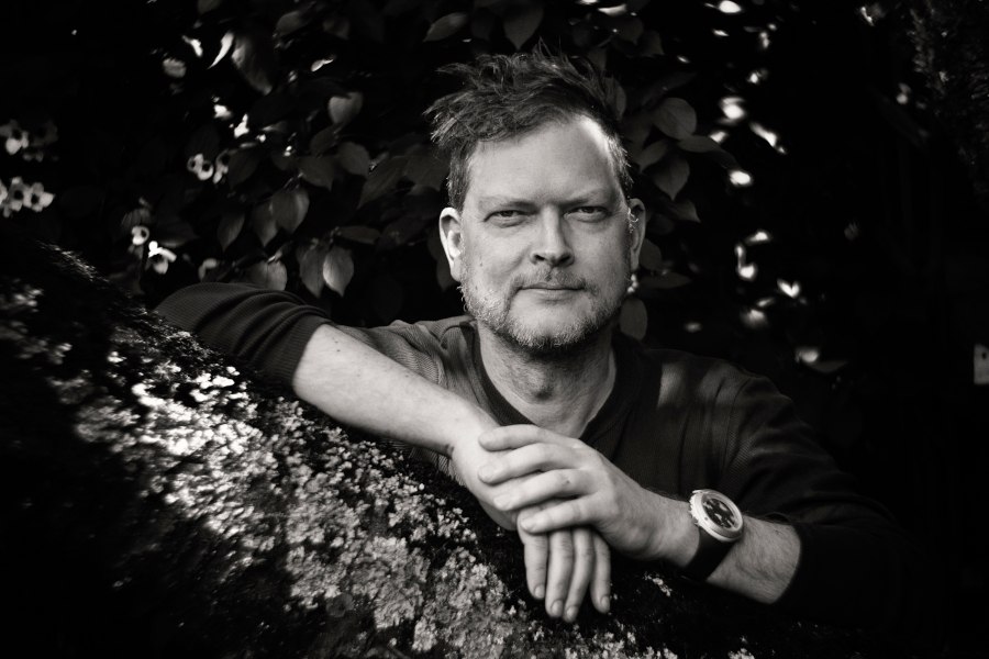 Ein Mann lehnt entspannt auf einem Baumstamm, umgeben von Bl&auml;ttern. Das Bild ist in Schwarz-Wei&szlig; gehalten und zeigt eine ruhige, nachdenkliche Stimmung., &copy; Foto: Ansgar Noeth