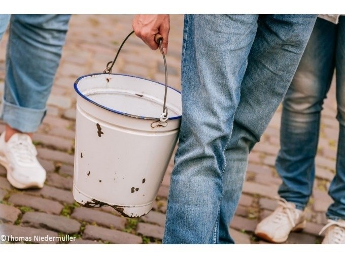 Person in Jeans trägt einen weißen Eimer auf Kopfsteinpflaster. Zwei weitere Personen sind teilweise sichtbar., © Stuttgart Marketing GmbH Person in Jeans trägt einen weißen Eimer auf Kopfsteinpflaster. Zwei weitere Personen sind teilweise sichtbar., © Stuttgart Marketing GmbH