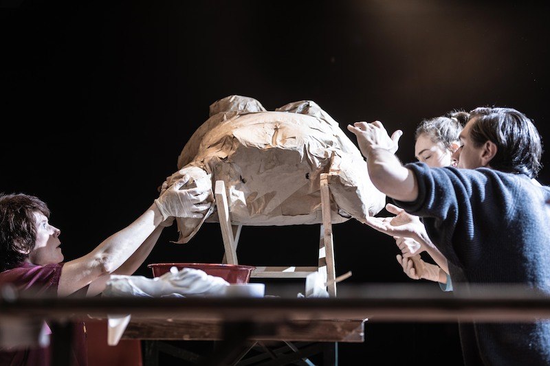 Drei Personen arbeiten an einer großen Papiermaché-Skulptur auf einem Tisch. Sie tragen Handschuhe und sind konzentriert., © Wilhelma Theater